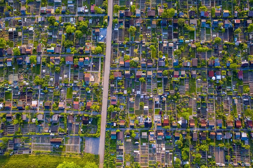 Vertikalni snimak iz zraka koji prikazuje detaljan raster katastarskih čestica s vrtovima i manjim objektima.